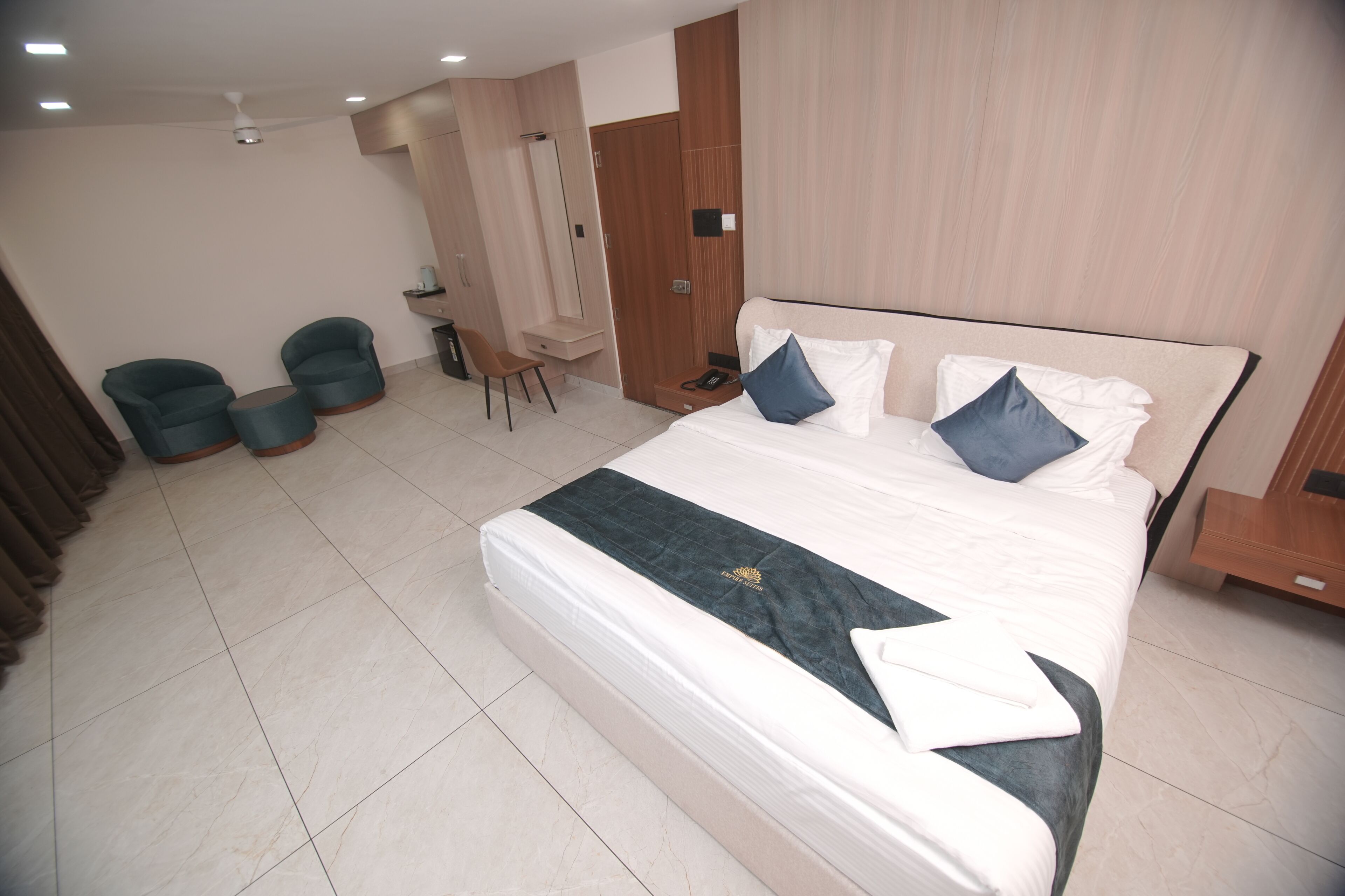 A hotel room with a large bed, two armchairs, a desk, and a wardrobe.