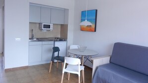 A compact kitchenette with a microwave, a small refrigerator, and a sink. There is a dining area with a table and two chairs. A blue sofa is positioned against the wall. - Studio in Tossa de Mar Near Beach & City Center (Tossa de Mar)