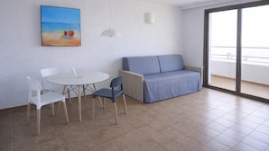 A room with a dining table, chairs, a sofa, and a large window with a view. - Studio in Tossa de Mar Near Beach & City Center (Tossa de Mar)