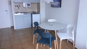 A compact kitchen with a microwave, stove, and sink. There is a dining table with four chairs. A painting hangs on the wall above the table. - Studio in Tossa de Mar Near Beach & City Center (Tossa de Mar)
