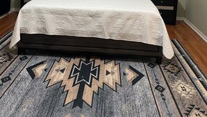Ein Schlafzimmer mit einem Bett, zwei Nachttischen, einem gemusterten Teppich und einem Deckenlüfter.