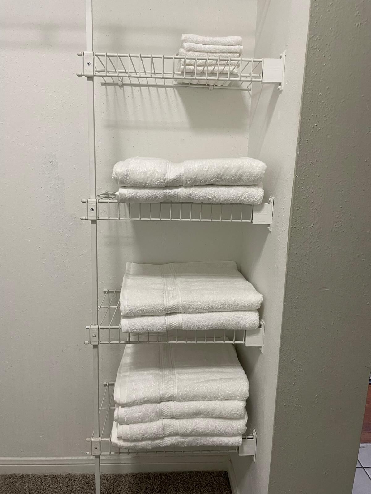 A white metal towel rack with three shelves holding folded white towels.