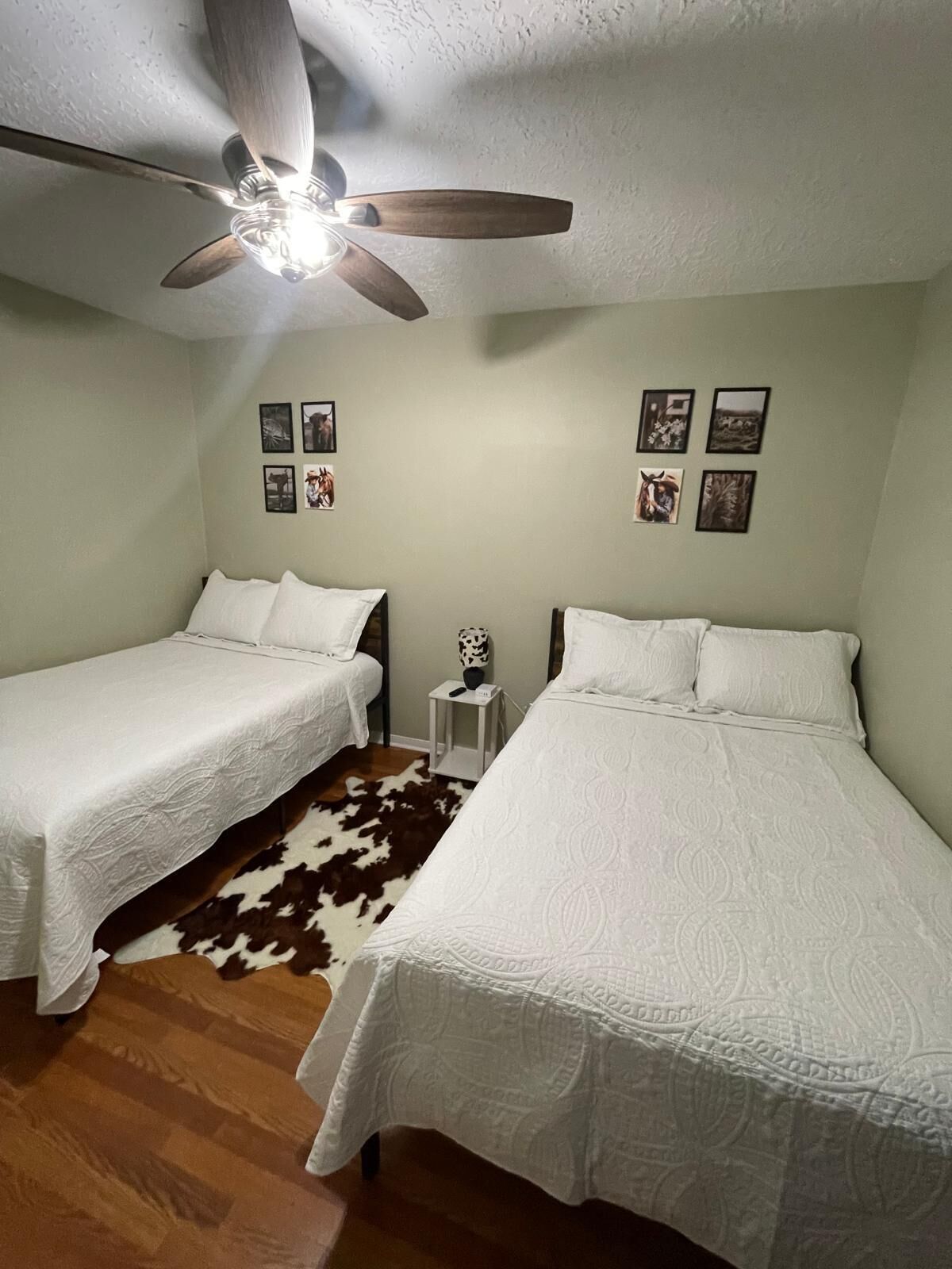 A room with two beds, a ceiling fan, and wall-mounted pictures.