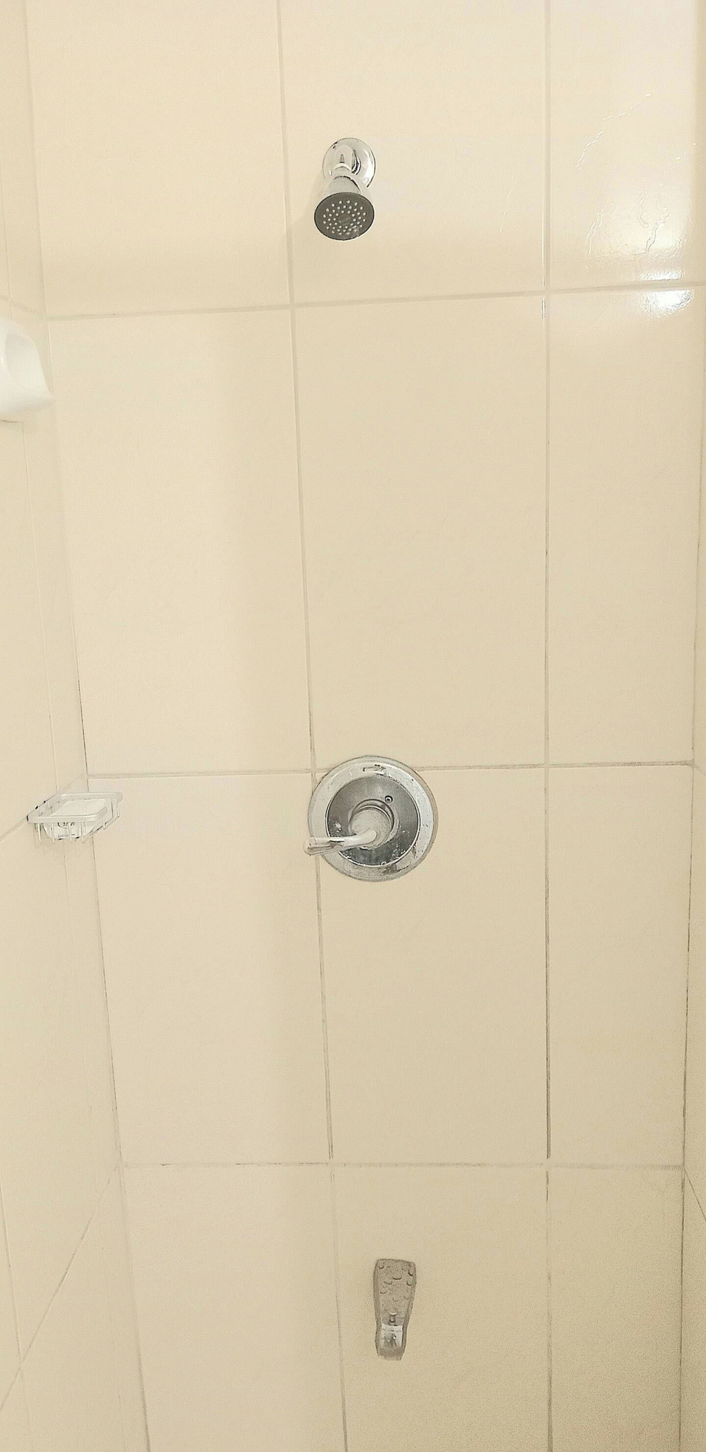 Un mur recouvert de carreaux, avec trois pommes de douche et une barre d’appui.
