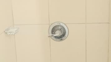 Un mur recouvert de carreaux, avec trois pommes de douche et une barre d’appui.