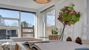 Ein Zimmer mit großem Fenster, einem Tisch mit Buch, einem Stuhl und einer Vase mit Blumen.