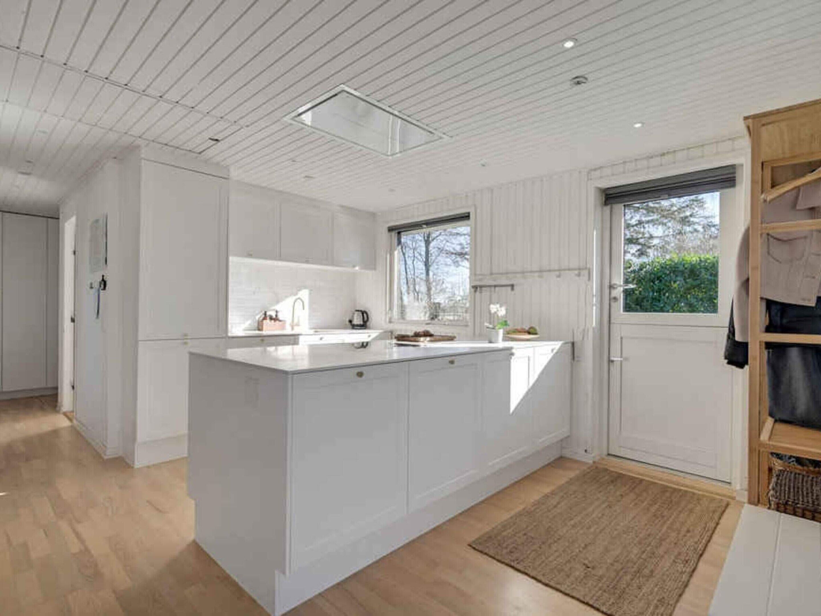 Una cocina moderna con armarios blancos, una isla central, una ventana y una puerta que da a un pasillo.