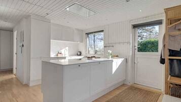 Una cocina moderna con armarios blancos, una isla central, una ventana y una puerta que da a un pasillo.