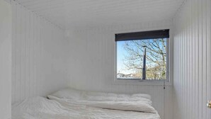 Ein Schlafzimmer mit Bett, Fenster und weißen Wänden.