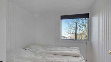 Un dormitorio con cama, ventana y paredes blancas.