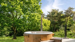 Ein hölzernes Whirlpool auf einer Terrasse mit Stufen, umgeben von üppiger Vegetation.