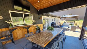 Une terrasse extérieure avec une table et des chaises en bois, un barbecue et un espace salon abrité.