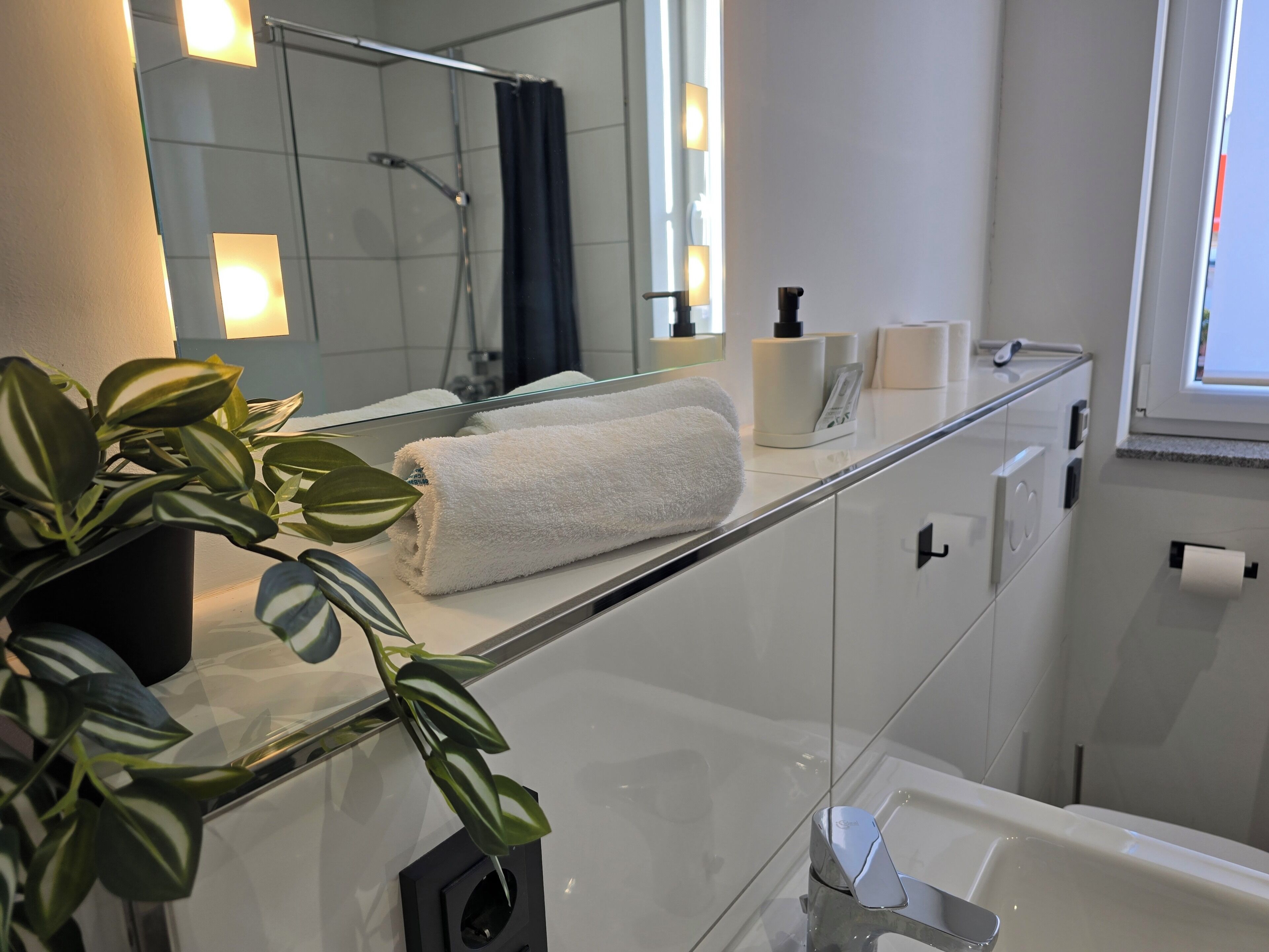 Een moderne badkamer met een douchecabine van glas, een witte handdoek op het aanrecht en een potplant.