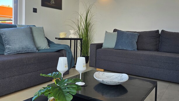 A modern living room with two grey sofas, a black coffee table, a white bowl, and two wine glasses. - Modern Apartment with Balcony near Airport (Siegburg)