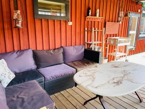 A wooden deck with a cushioned seating area, a table, and a hanging lantern. - 6 Person Holiday Home in Kosta (Kosta)