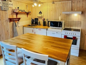 A compact kitchen with wooden walls, a wooden table, white cabinets, a microwave, a stove, and a sink. - 6 Person Holiday Home in Kosta (Kosta)