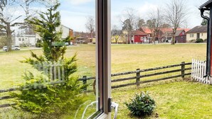 A view through a window of a grassy area with a wooden fence, a small tree, and houses in the background. - 6 Person Holiday Home in Kosta (Kosta)