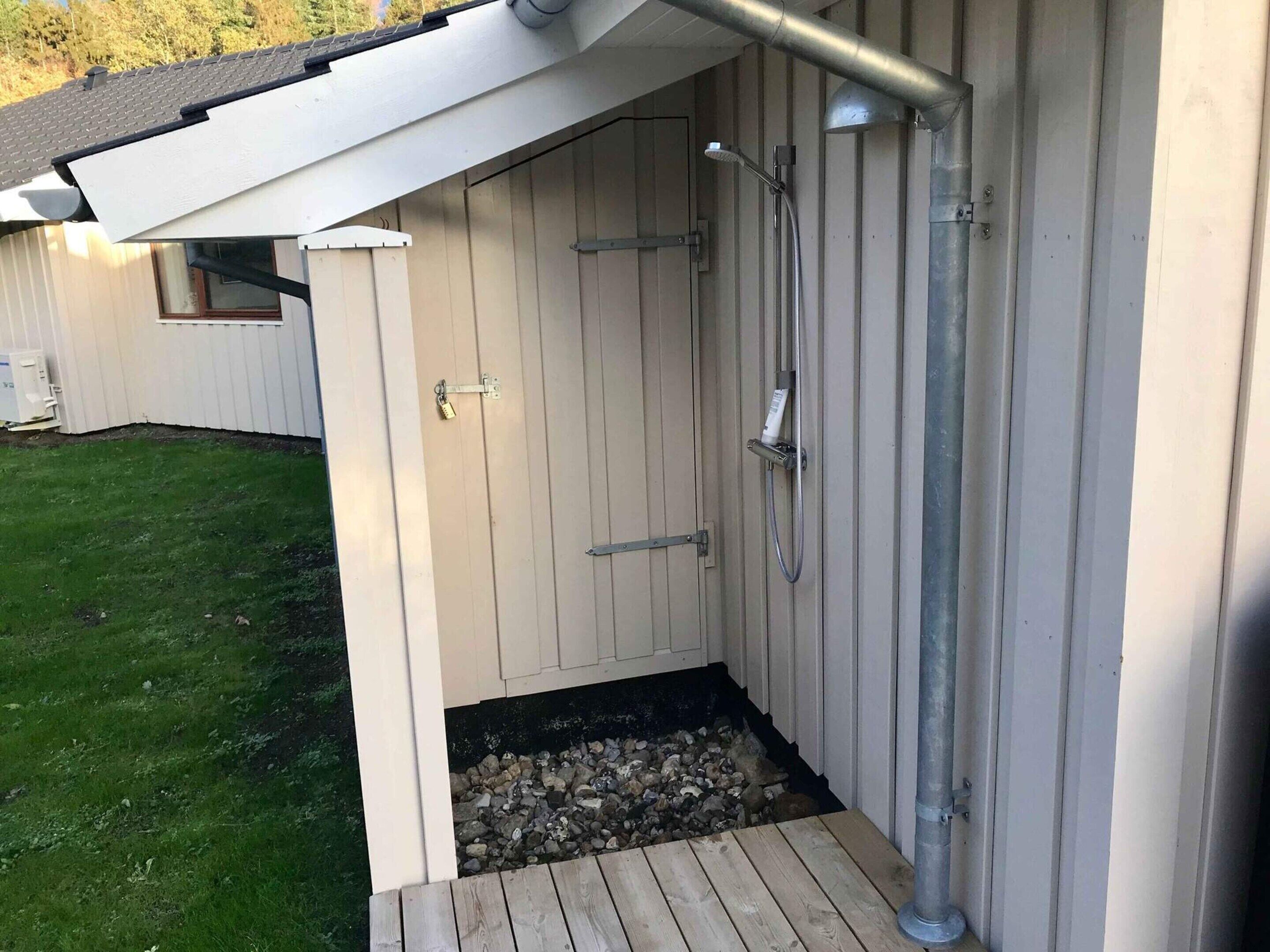 A wooden outdoor shower enclosure with a metal pipe, a wooden deck, and a grassy yard.