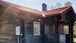 Una cabaña de madera con porche, chimenea y una ventana.
