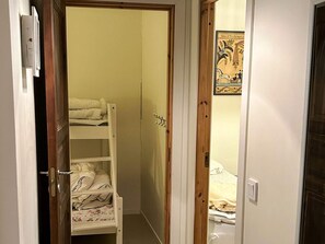 Un couloir étroit mène à une pièce où se trouve un lit superposé et une porte dotée d’un cadre en bois.