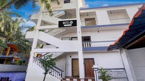 A multi-story hotel with a sign indicating it offers complete services, a staircase leading to the entrance, and a view of the surrounding area including palm trees. - Saver Double Bella's Residency (Calangute)