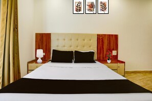 Une chambre d’hôtel avec un grand lit, deux tables de chevet, une petite table, une lampe et des œuvres d’art encadrées accrochées au mur.