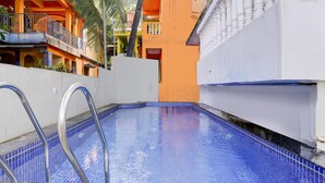 A swimming pool with metal railings, surrounded by a white wall and an orange building with balconies. - Saver Double Bella's Residency (Calangute)