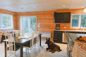 A wooden interior with a dining area, a kitchen, and a dog sitting on the floor. - Chalet 3M & Spa - Lanaudiere (Chertsey)