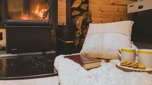 Una stanza accogliente con una stufa a legna, un divano confortevole, un libro e due tazze su un sottobicchiere di legno.