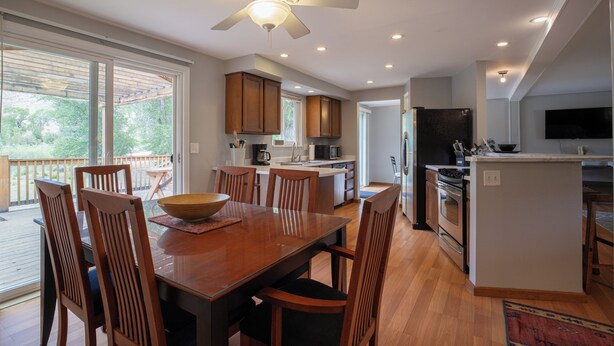 A modern kitchen with wooden cabinets, a dining area with a large table and chairs, and a ceiling fan.