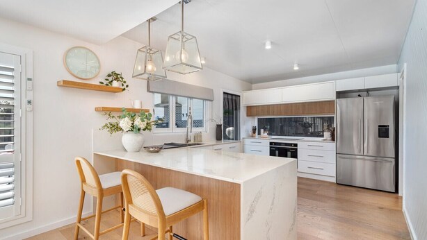 A modern kitchen with a marble island, wooden chairs, stainless steel appliances, and pendant lighting. - Coastal Waterfront Broadbeach Waters (Broadbeach Waters)