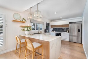 Una cocina moderna con una isla de mármol, sillas de madera, electrodomésticos de acero inoxidable e iluminación colgante.