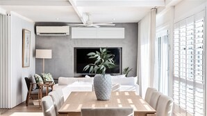 A modern living room with a sofa, a dining table, and a TV mounted on the wall. - Coastal Waterfront Broadbeach Waters (Broadbeach Waters)