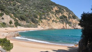 A beach with clear turquoise water, sandy shore, and a rocky hillside in the background. - Apartment Inmas Nou With Shared Pool (Castell-Platja d'Aro)
