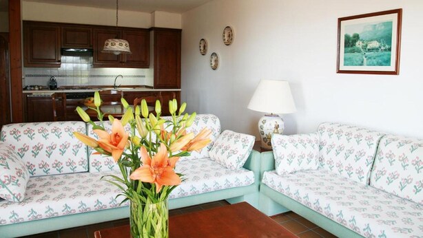 A living room with a sofa, a coffee table with flowers, a lamp, and a kitchen in the background. - Apartment Inmas Nou With Shared Pool (Castell-Platja d'Aro)