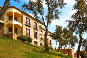 A multi-story building with balconies, stone walls, and a grassy hill. - Apartment Inmas Nou With Shared Pool (Castell-Platja d'Aro)
