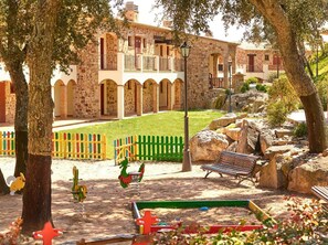 A courtyard with stone buildings, a green lawn, and a bench. - Apartment Inmas Nou With Shared Pool (Castell-Platja d'Aro)