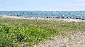 A beach with a rocky breakwater, grassy areas, and a clear view of the ocean. - 4 Star Holiday Home in Dannemare (Dannemare)