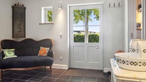 A room with a dark-colored sofa, a white door with a window, and a tiled floor. - 4 Star Holiday Home in Dannemare (Dannemare)