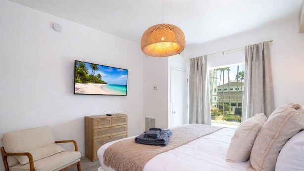 A bedroom with a bed, a chair, a dresser, a television, and a window with curtains. - Relaxing and charming 1Bd/1Bh Retreat  - FREE Shuttle (Orlando)