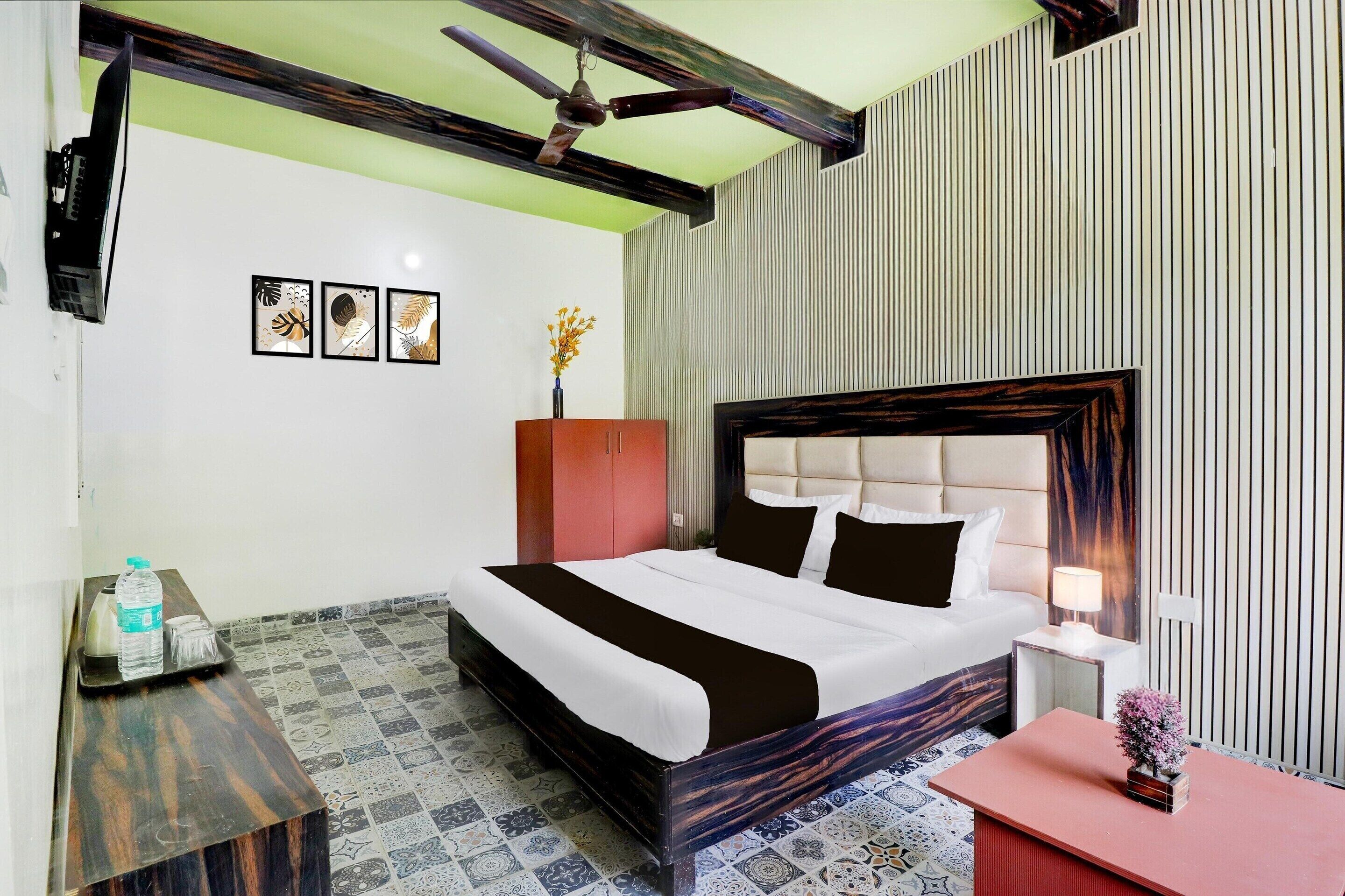 A hotel room with a bed, a nightstand, a desk, a chair, a ceiling fan, and a wall with vertical lines.