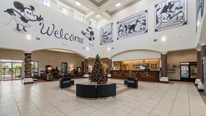 Een ruime lobby met een kerstboom in het midden, een receptiebalie en afbeeldingen van Mickey Mouse in lijsten aan de muren.
