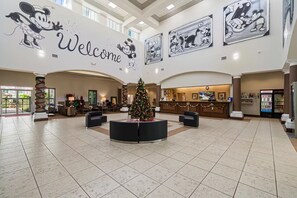 A spacious lobby with a central Christmas tree, a reception desk, and framed Mickey Mouse artwork on the walls. - Inspiring and cozy Botanic Retreat - FREE Shuttle (Orlando)