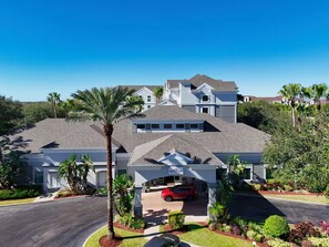 A multi-story residential building with a covered driveway, palm trees, and a red car parked in the driveway. - Inspiring and cozy Botanic Retreat - FREE Shuttle (Orlando)