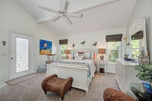 A bedroom with a bed, two nightstands, a ceiling fan, a window with blinds, a door, and a painting on the wall. - Steps to Beach - Anna Maria Island - Island Time! (Anna Maria)