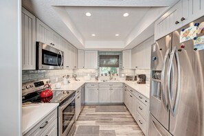 A modern kitchen with white cabinetry, stainless steel appliances, and a tiled backsplash. - Steps to Beach - Anna Maria Island - Island Time! (Anna Maria)