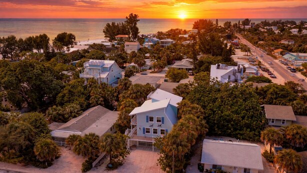 Zona residencial costera con casas, palmeras y un atardecer.