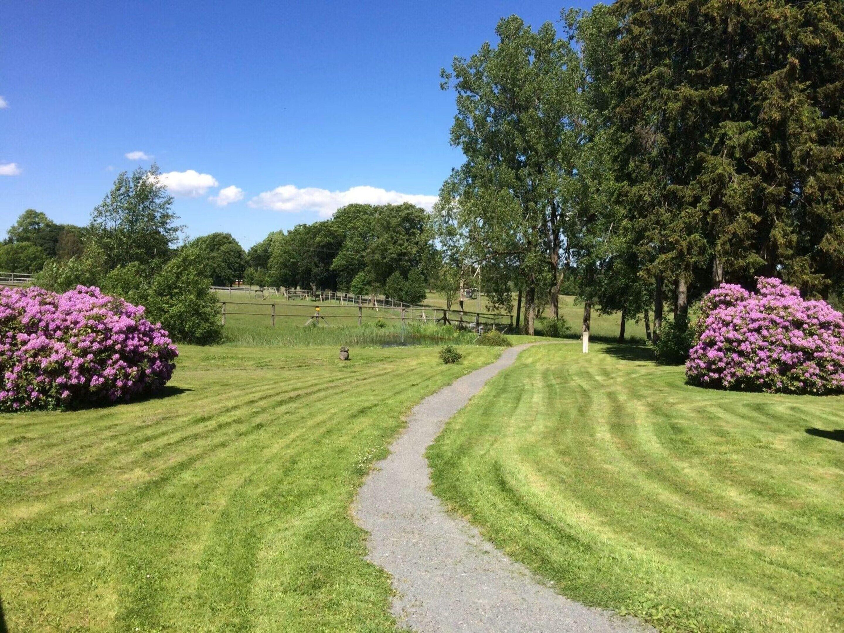 A well-maintained grassy area with a gravel path, surrounded by trees and shrubs.