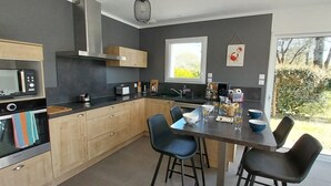Uma cozinha moderna com forno embutido, micro-ondas e pia, armários de madeira e uma área de refeições com cadeiras.