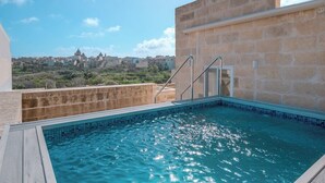 A rooftop swimming pool with a stone wall and a view of a cityscape.
